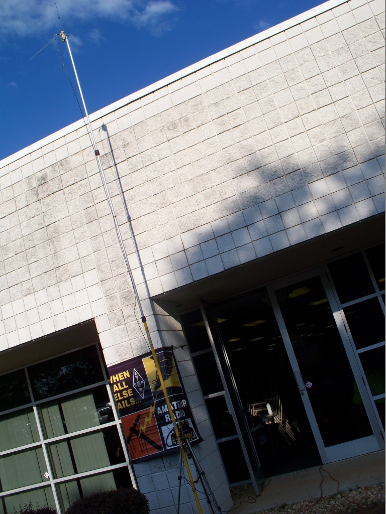 A 20 foot tall painter's pole holding a dual band ground plane antenna with a ARES banner in the background.