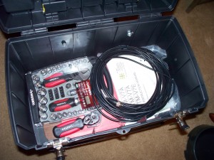 A roll of coax, a box of tools, some paper forms all stored inside a large toolbox.