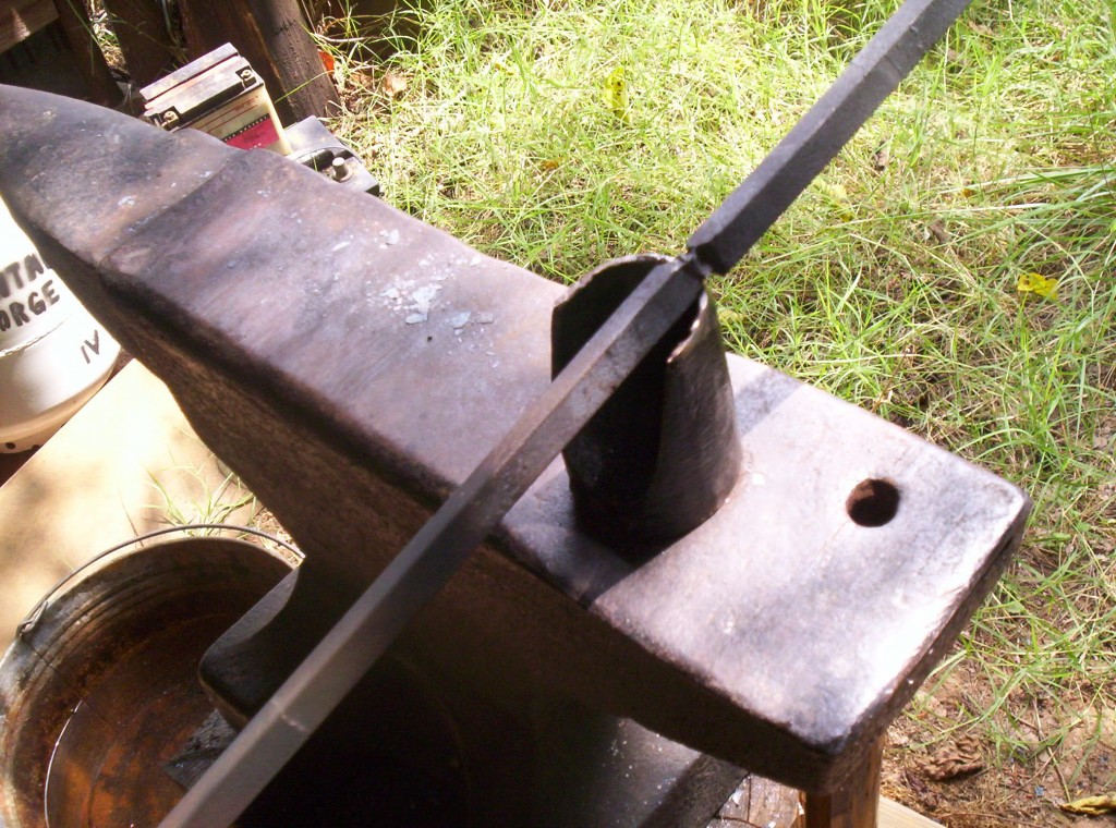 The stock is placed across a tool that is sitting on the anvil. A groove is cut around the stock.