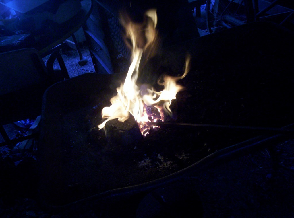 An extremely bright fire leaps a foot above the coals, the end of the stock is tucked under the coals.