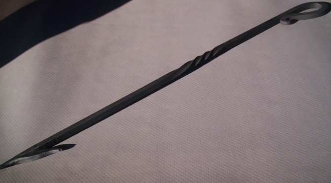 The fire hook laid out in a display. One end is pointed with a hook portion that sticks out about thirty degrees, the twist is in the middle, and the curved handle with pig-tail.