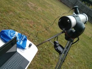 A telescope, table and laptop set up in the backyard.