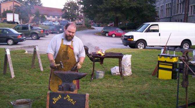 Geof hammering metal at the anvil. In the background the coal fire smokes merrily.