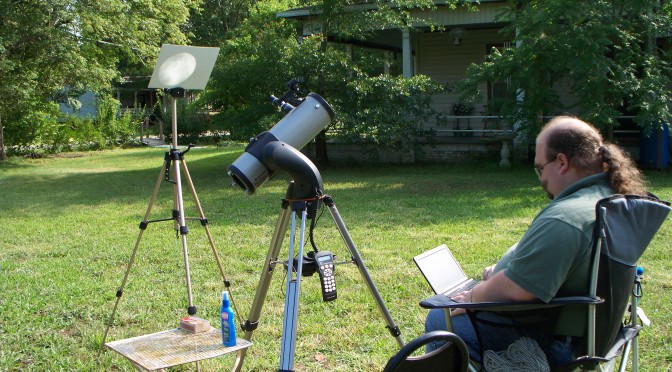 Geof using a netbook while in the background a telescope projects an image of the sun on a piece of white posterboard.