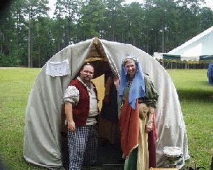 Geof and Barbara stand infront of their bender tent, dressed in their garb.